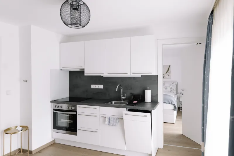 Modern fehér konyha beépített sütővel és sötét hátfallal